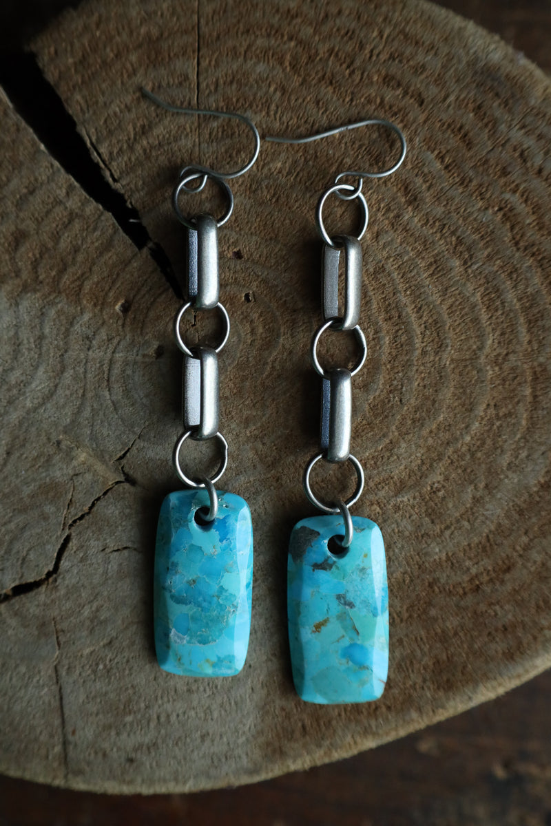 Turquoise earrings with silver chains on a wooden surface