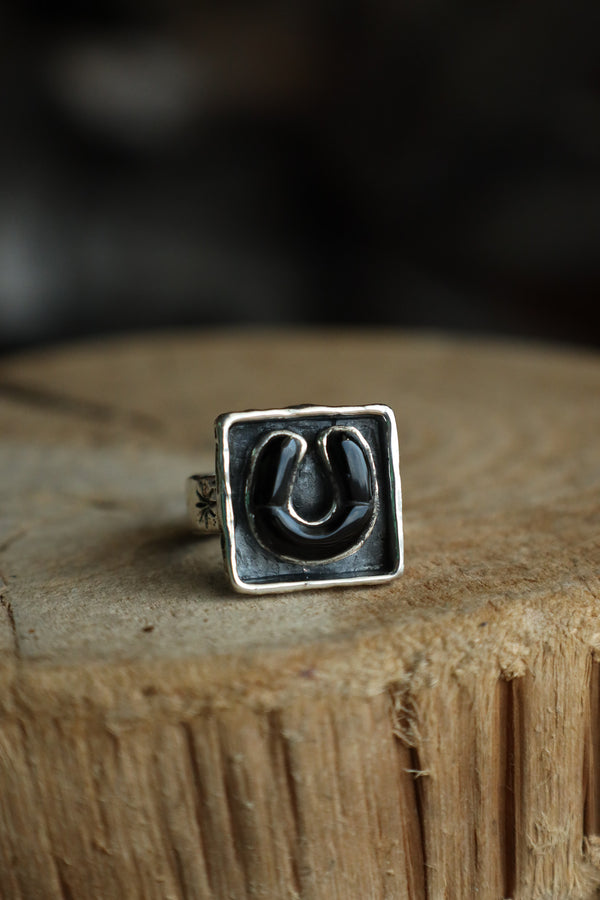 Silver ring with a black square design on a wooden surface