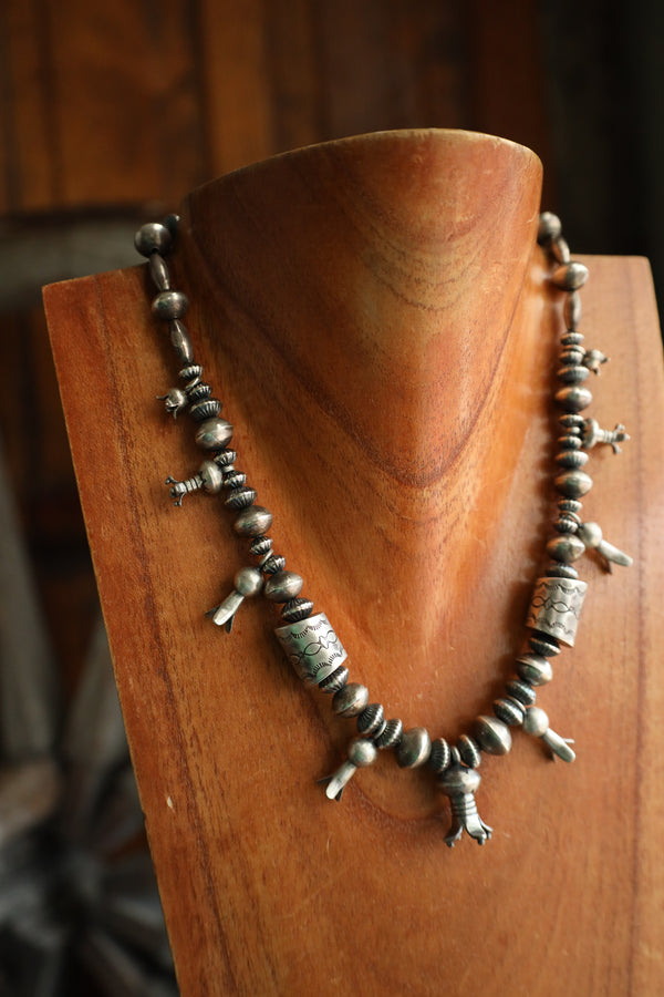 Silver beaded necklace on a wooden stand with a blurred background