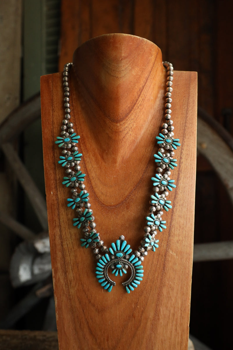 Turquoise and silver necklace on a wooden stand with a rustic background