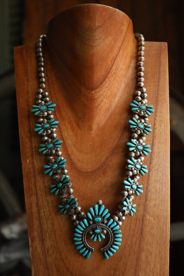Turquoise and silver beaded necklace on a wooden stand