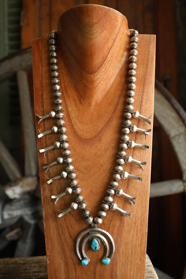 Silver beaded necklace with turquoise stones on a wooden stand