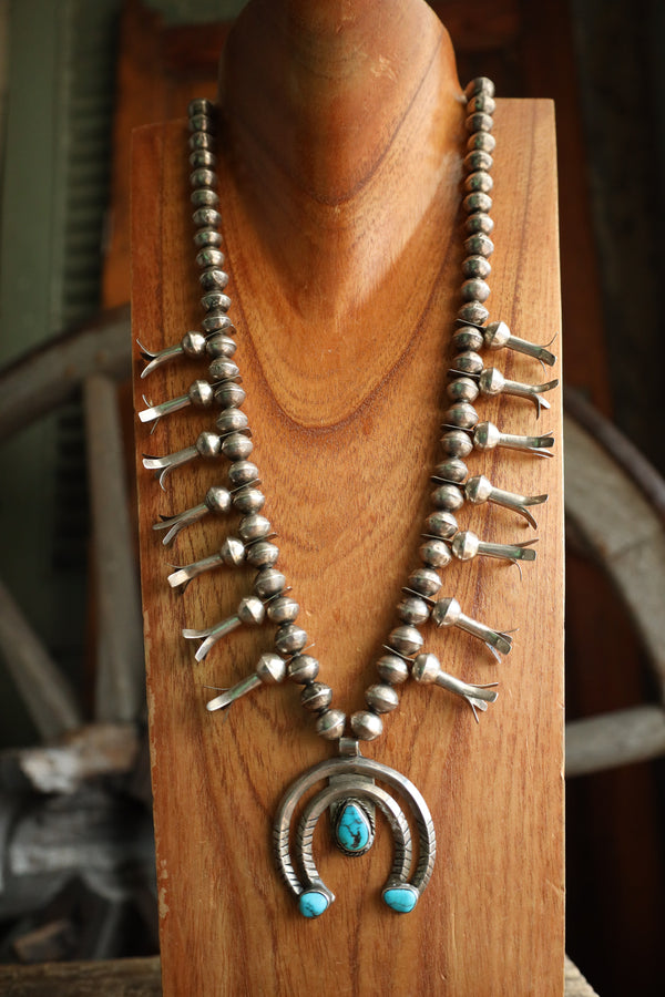 Silver necklace with turquoise stones on a wooden stand