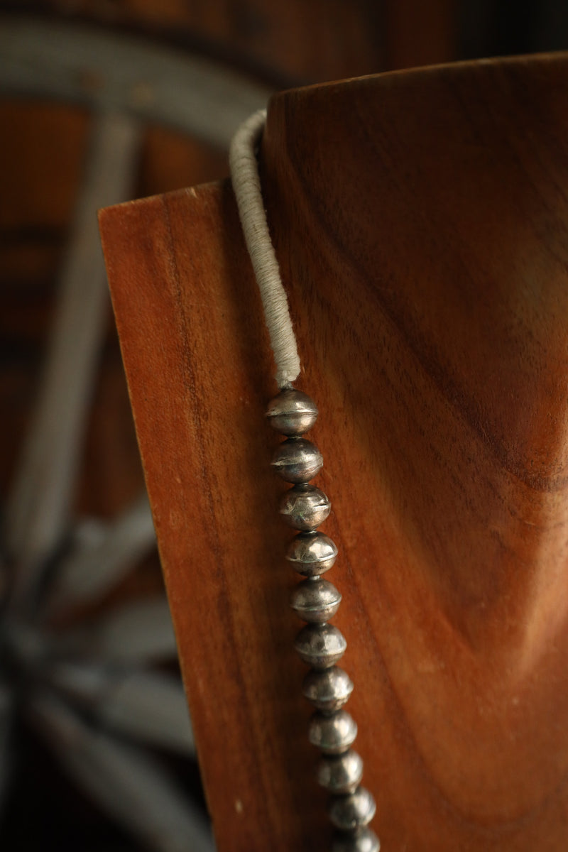 Close-up of a wooden object with a beaded string, possibly a prayer wheel, in a blurred background.