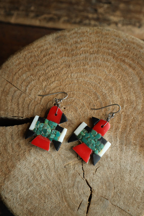 Pair of earrings with red, green, and black geometric design on a wooden surface