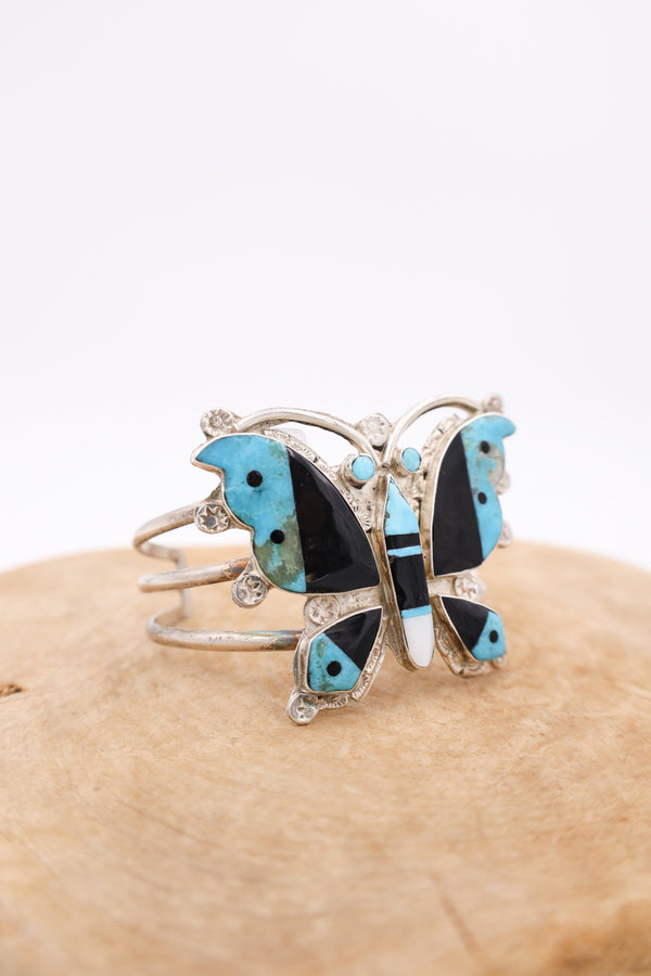 Vintage butterfly bracelet cuff with turquoise, mother of pearl and onyx inlay, sitting on wood display