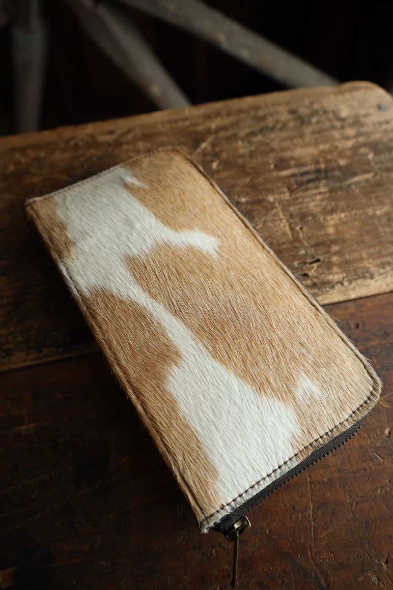 Brown and white cowhide leather wallet on a wooden surface