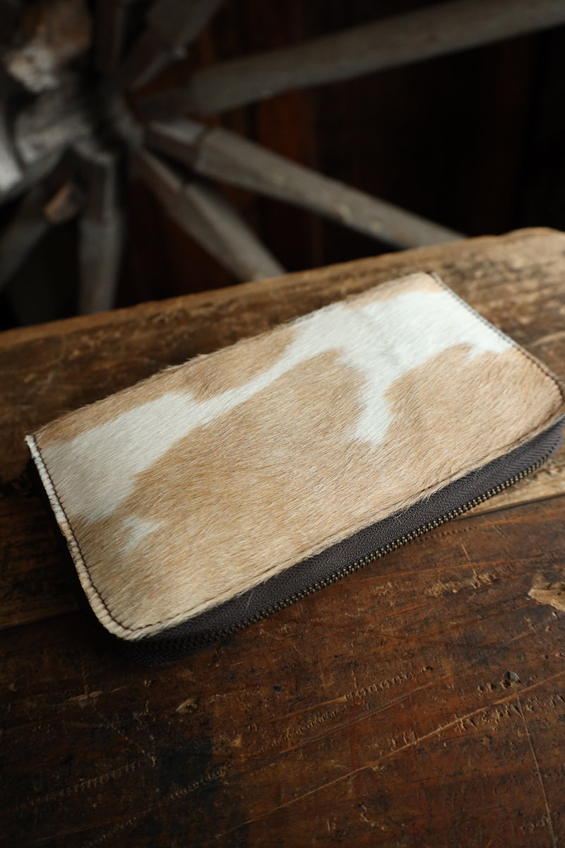 Brown and white cowhide wallet on a wooden surface with a rustic background
