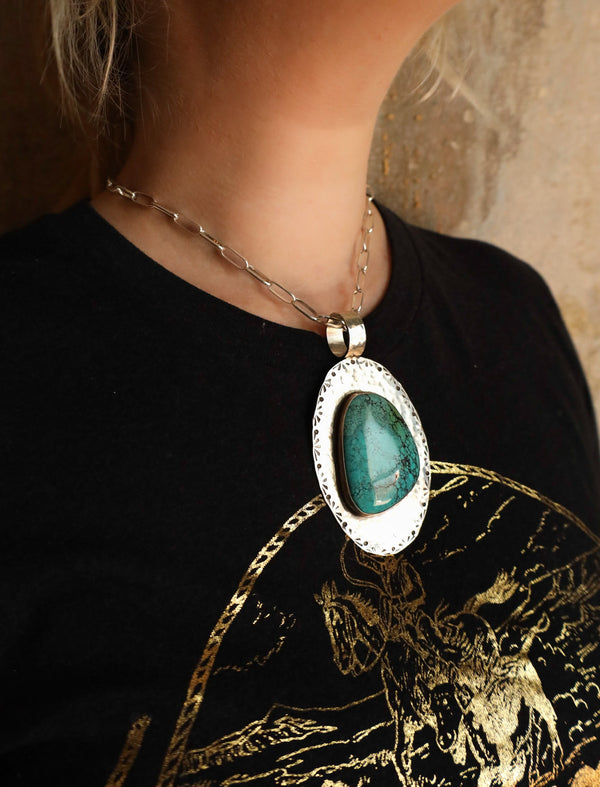 Woman wearing turquoise gem pendant set in a sterling silver bezel and mounted on a hammered sterling silver oval base