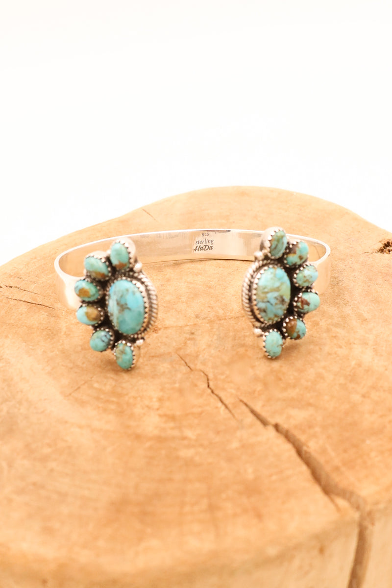 Two turquoise and brown half flowers flanking either side of a sterling silver cuff