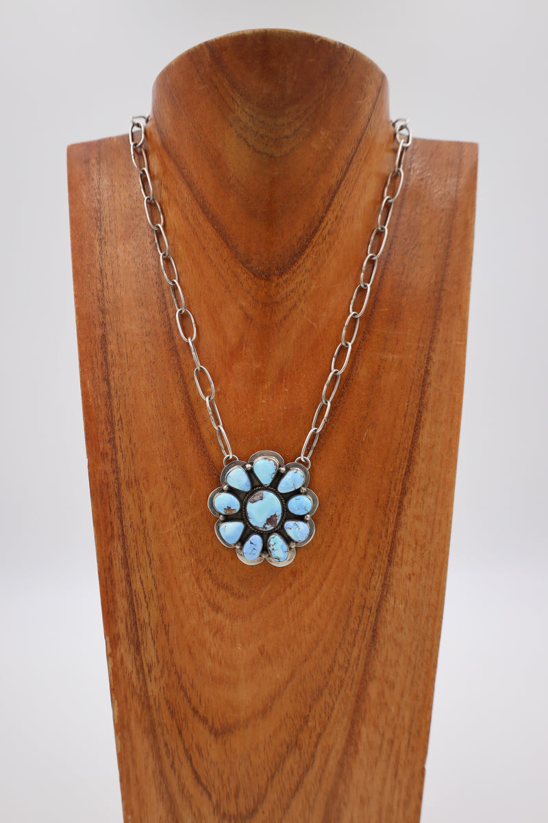 Turquoise necklace in the shape of the flower set in sterling silver. This necklace is hanging on a wooden display neck.