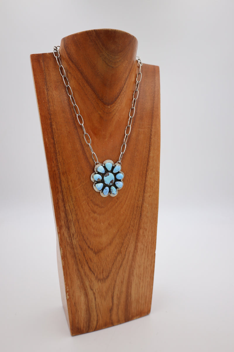 Turquoise necklace in the shape of the flower set in sterling silver. This necklace is hanging on a wooden display neck.