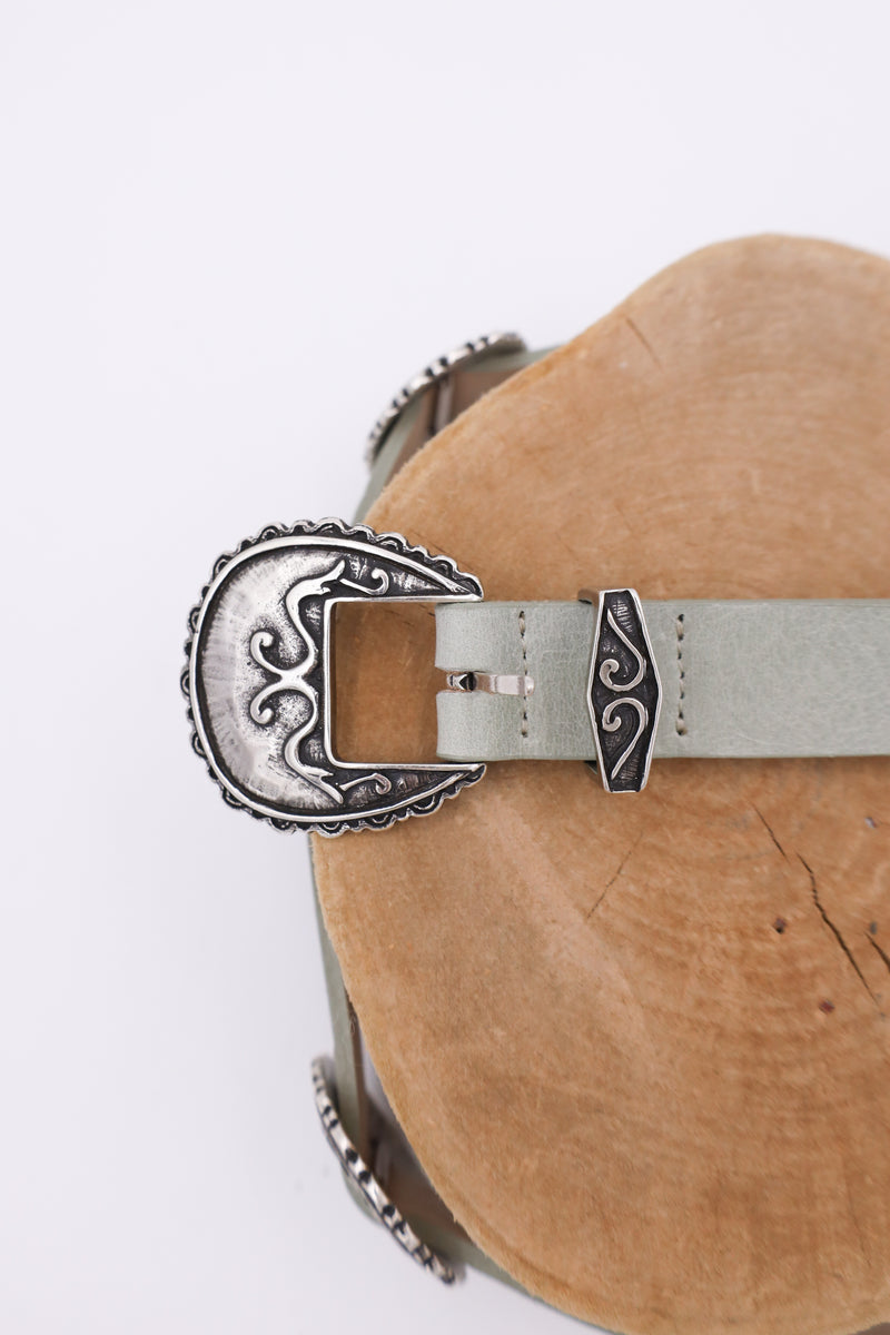 Sage leather belt with silver conchos on it