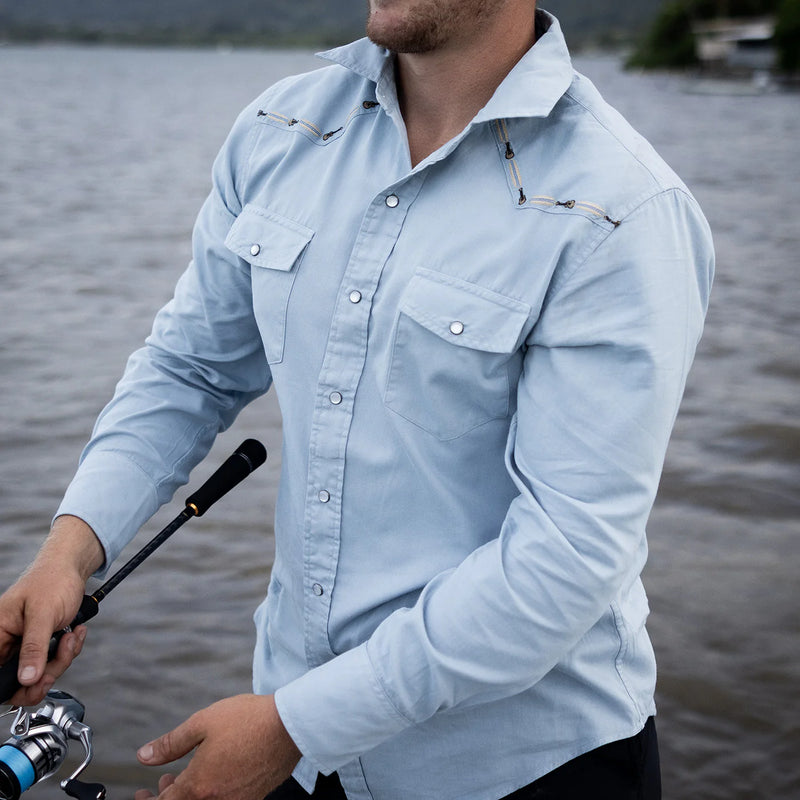 Person wearing a light blue denim shirt by a body of water
