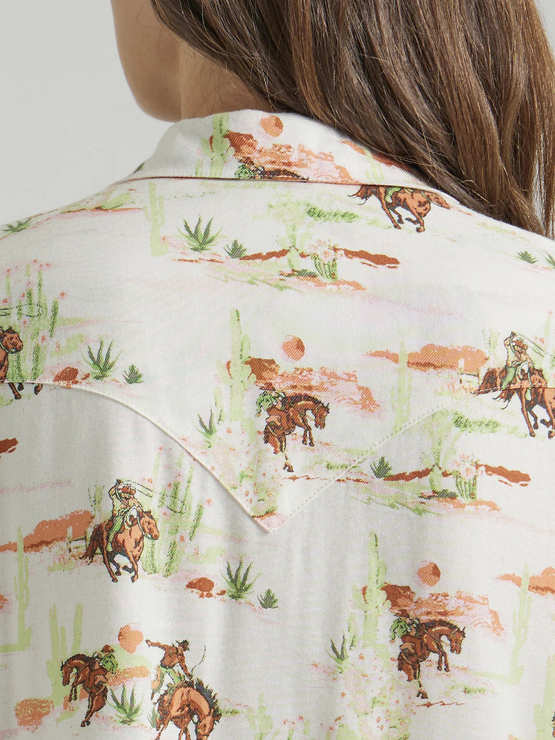 woman wearing short sleeve button front shirt with images of cowboys riding horses in the desert