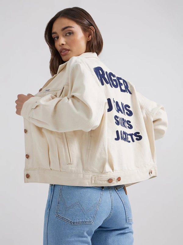 Woman wearing white denim jacket with words "Wrangler jeans shirts jackets" on the back in navy