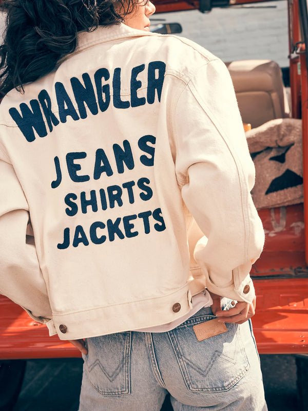 Woman wearing white denim jacket with words "Wrangler jeans shirts jackets" on the back in navy