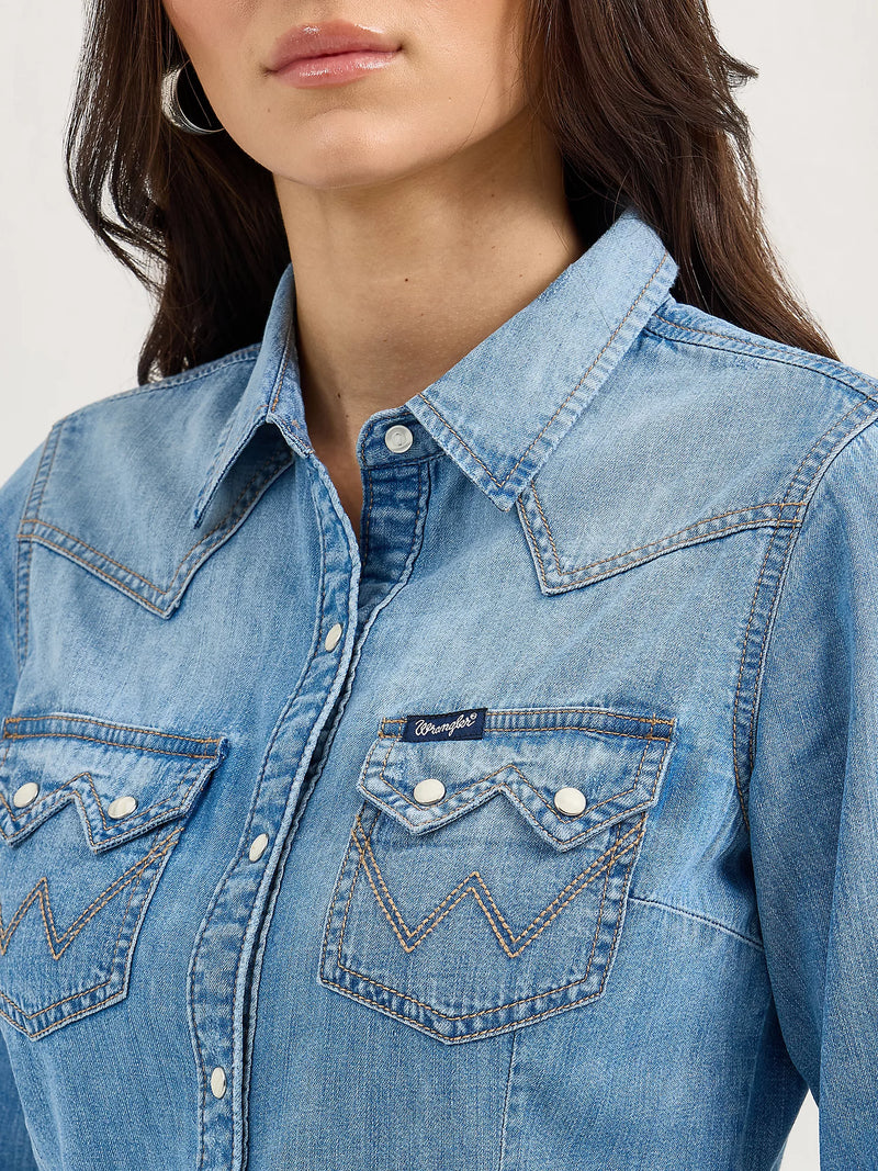 Close-up of a person wearing a blue denim shirt with a brand logo.