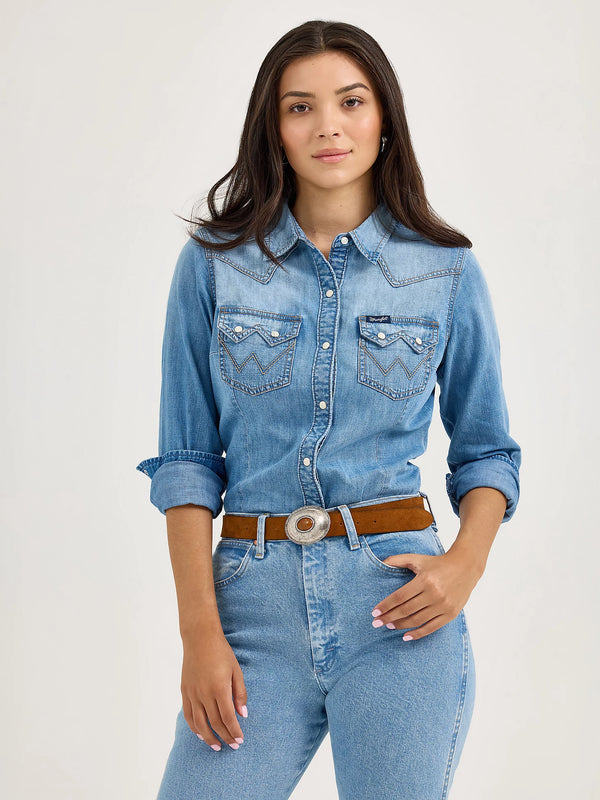Woman wearing a blue denim shirt and jeans with a belt on a light gray background