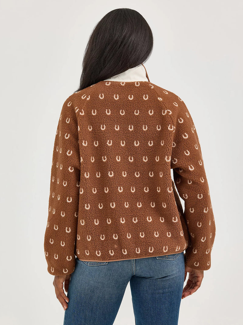 Person wearing a brown sweater with a pattern, standing against a plain background