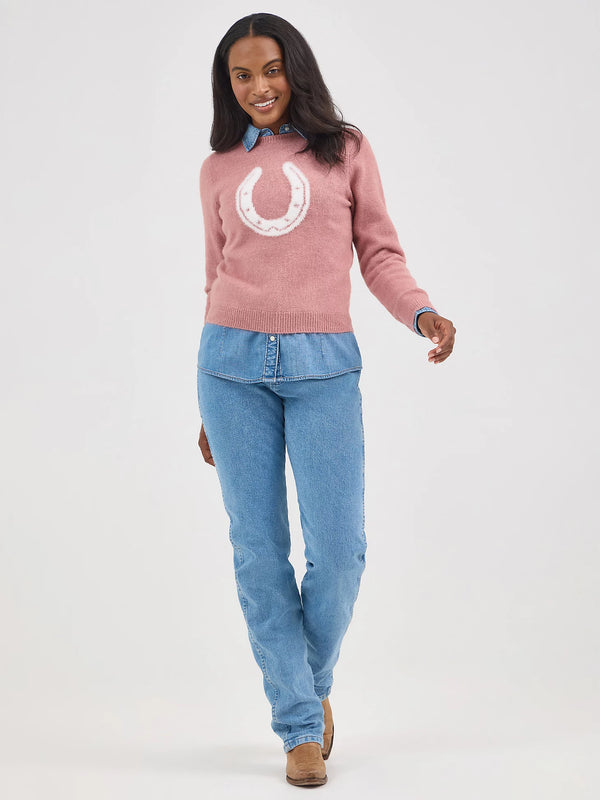 Woman wearing a pink sweater with a white horseshoe design and blue jeans on a white background