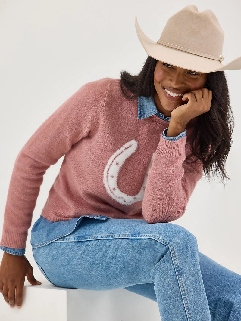 Woman wearing a pink sweater with a horseshoe design and a beige cowboy hat.