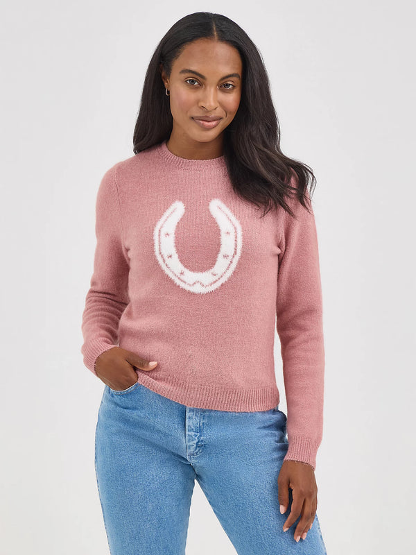 Woman wearing a pink sweater with a white horseshoe design on a plain background