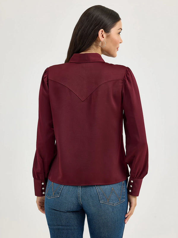 Woman wearing a burgundy blouse with long sleeves and blue jeans on a white background