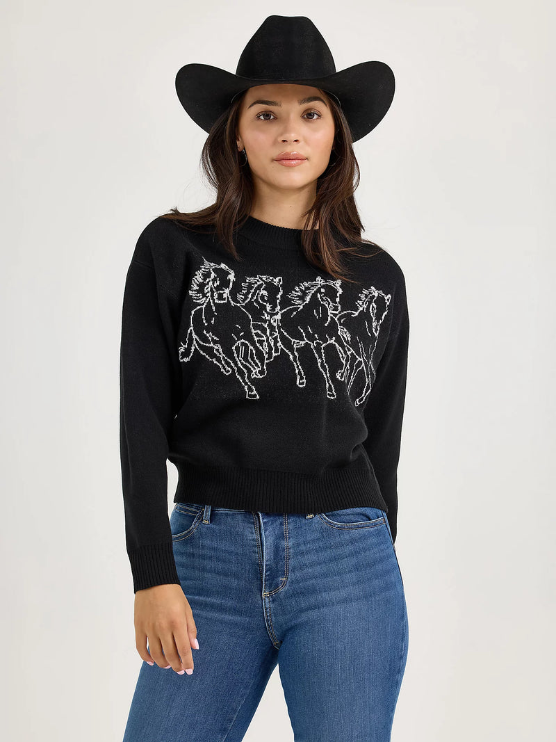 Woman wearing a black sweater with horse design, blue jeans, and a black cowboy hat on a white background