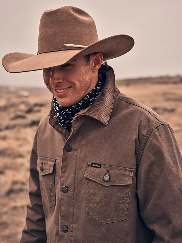 Man wearing a brown cowboy hat and jacket with a bandana in a desert setting