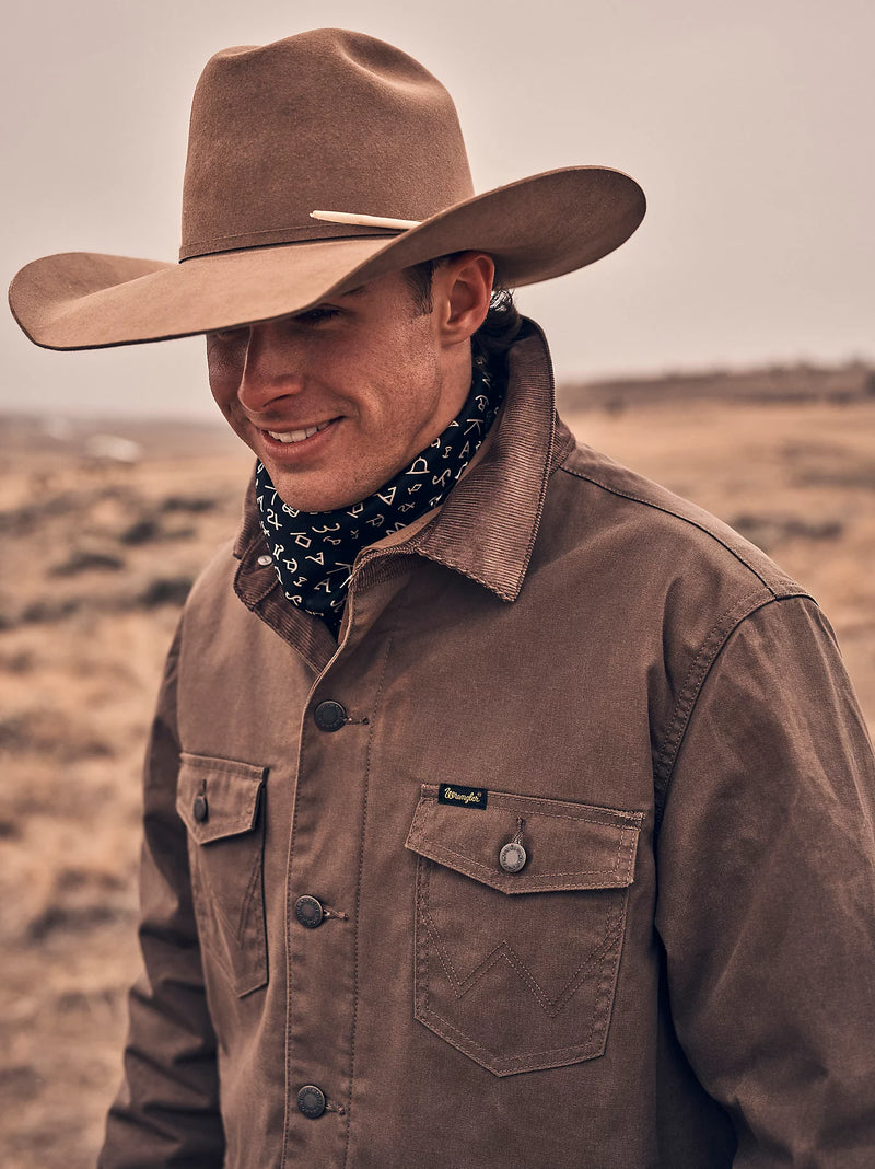 Man wearing a brown cowboy hat and jacket with a bandana in a desert setting