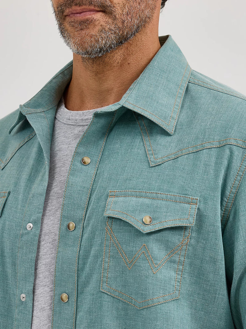 Teal denim shirt with a pocket detail worn by a person on a light gray background
