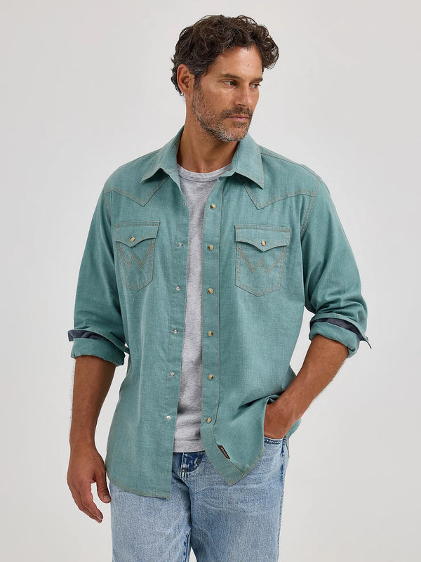 Man wearing a teal denim shirt over a gray t-shirt with blue jeans on a white background