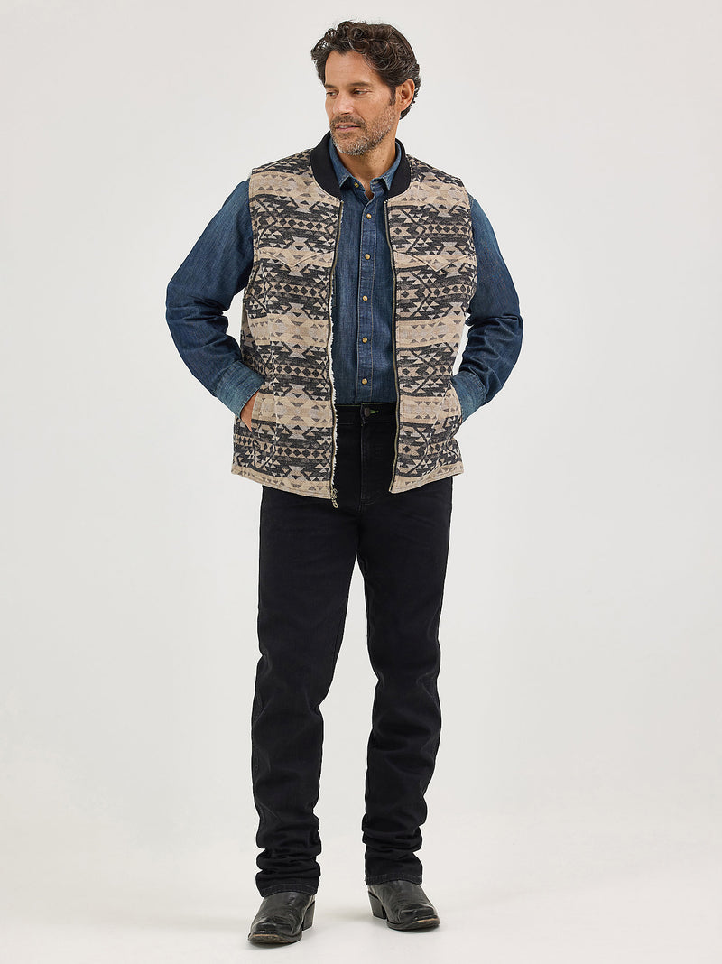 Man wearing a patterned vest over a denim shirt on a white background