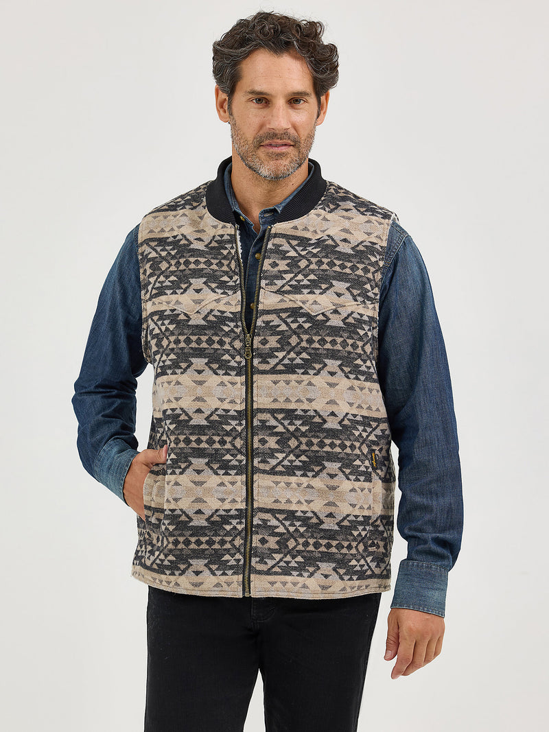 Man wearing a patterned vest over a blue shirt on a white background