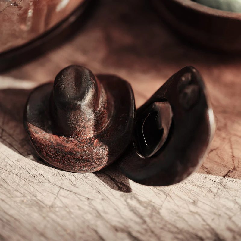 Close-up of a dark brown ceramic object on a textured surface