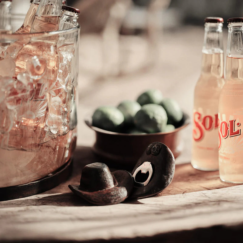 Bottles of SoCoL drink on a wooden surface with limes and a cowboy hat.