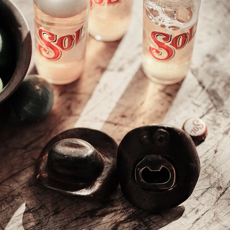 Two bottle openers on a wooden surface with Sol bottles in the background.