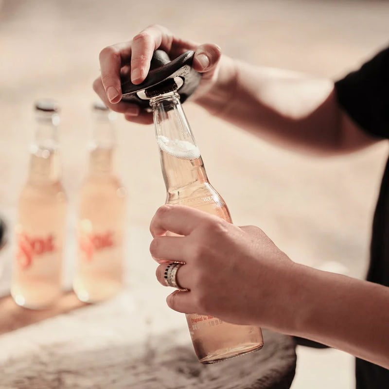 Person opening a bottle of pink sparkling wine with a blurred background