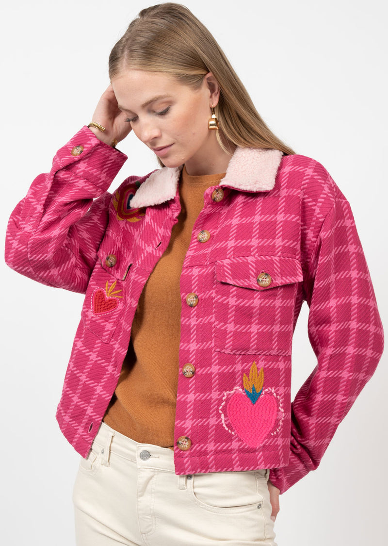 Woman wearing pink tweed jacket with embroidered heart with crowns