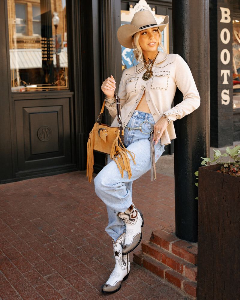 Woman in cowboy hat and boots posing in front of a store with 'Boots' sign.