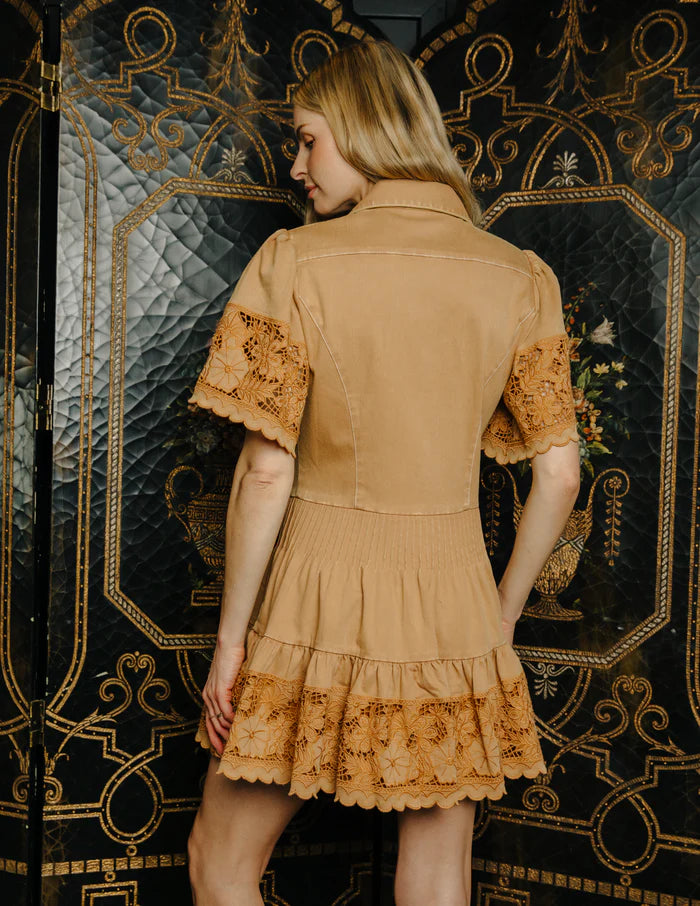 Woman wearing a beige dress with lace details in front of an ornate black and gold wall.