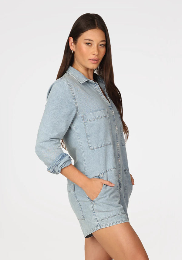Woman wearing denim long sleeve romper with button front and functional pockets on side and breast