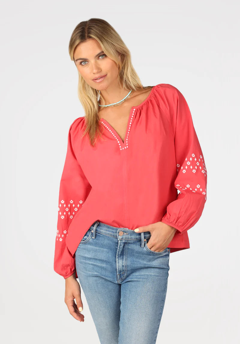 Woman wearing red long sleeve pilgrim top with v neck, and eyelet details on the sleeves 