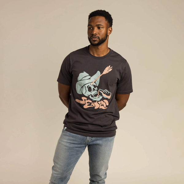 SENDERO TIRO MUERTO T-SHIRT Black. Graphic image of a skull with a cowboy hat and arrow stuck to its forehead drinking from a soda or beer bottle and a liquid font of Sendero under the skulls neck