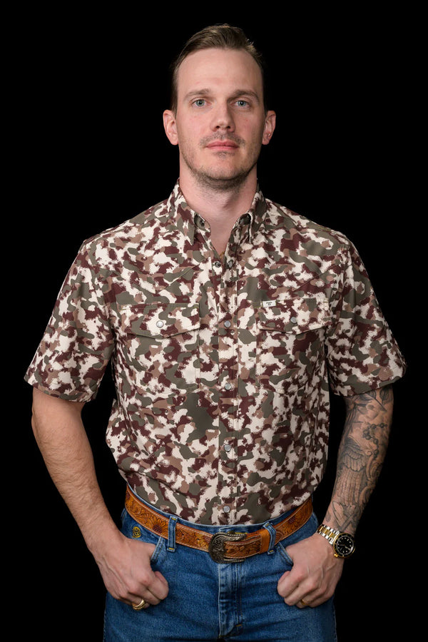 Man wearing a camouflage shirt and jeans against a black background