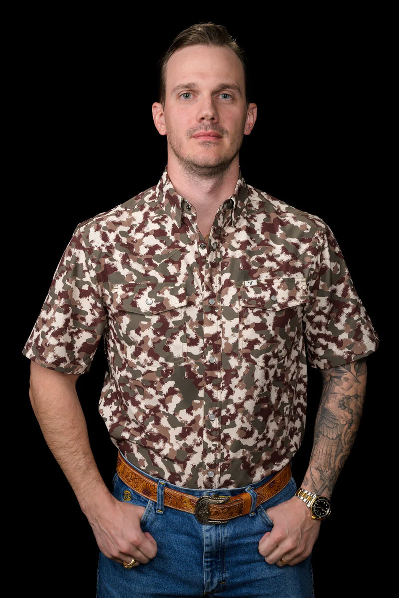 Man wearing a camouflage shirt and jeans against a black background