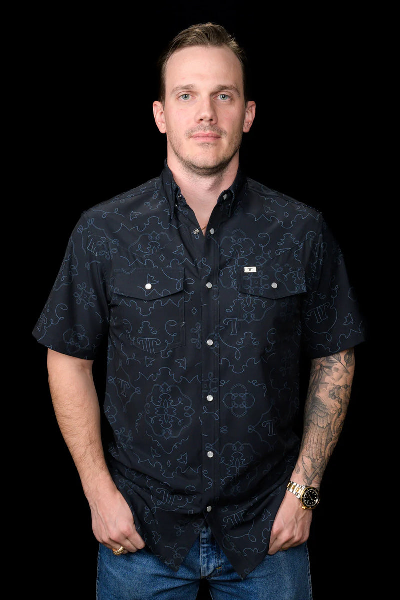 Man wearing a dark patterned shirt against a black background