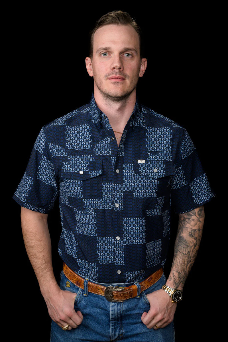 Man wearing a navy patterned shirt and jeans against a black background