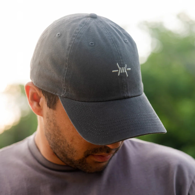 Man wearing a dark blue cap with a logo, outdoors with blurred greenery in the background